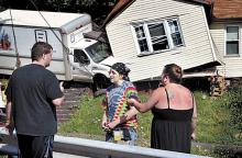 Joe Baluski, left, 34, was asleep on a sofa under the three windows in the house on Butler Court in Shickshinny, in the background, when a box truck crashed into him home on Wednesday morning.(Press Enterprise/Bill Hughes) 