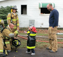 Brian Nevel, right, watches as his son Carter, 3, exchanges a high-five with Jonathan Shannon, a volunteer with Espy Fire Co., while Cody Fronk, another volunteer, looks on. The firefighters had just finished dousing a blaze on Third Street in Mifflinville. Carter, who lives across the street, put on his firefighter's costume and came over to help. (Press Enterprise/Susan Schwartz)