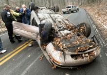 Espy Rescue Chief Dana Shaffer steadies driver Dane Albertson, 50, of Orangeville, after helping him out of his overturned car on Fifth Street Hollow Friday. Sgt. Joe Grassley, far left, and Police Chief Ray Klingler, take notes at the crash scene.