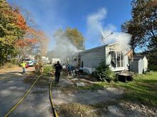 A firefighter prepares to vent the roof while fighting a fire in a trailer home at 2 Rhodes Street in Almedia Tuesday afternoon.
