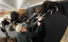 Scott Gulliver, left, gives direction to Zach Clossen as Clossen holds up a mount with two fishers on it that Gulliver created and is displaying at his booth, Gulliver's Taxidermy of Walpwallopen, at the Early Bird Sports Expo at the Bloomsburg Fairgrounds.