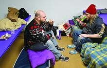Tyler Bradsley, left, and Hayden Steimling sit on their cots in the lunchroom at AGAPE Tuesday night while having something to eat. The friends are staying at the shelter during the code blue because of being homeless. 