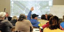 A man in the crowd at the public meeting for the Riverside railroad crossing replacement project at St. Peter's Fellowship Hall in Riverside holds his hand up to ask a question of the representatives gathered at the meeting.