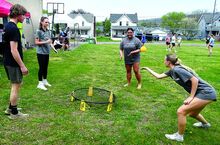 A teenage girl playing Spikeball tosses a ball into a low net as other teens look on.