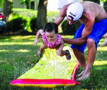 Maya Liddick, left, 1, is lifted over water spraying from a Slip N' Slide by her uncle Mitchell Liddick outside their Espy home Tuesday afternoon. It was the girl's first time on the summer slide.