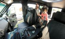 Leonard Rogutski, a team leader with the Columbia-Montour S.W.A.T., sits in the BearCat with Isaac Sysko, 3, who was getting a closer look at the police response vehicle during the police National Night Out program in Berwick Tuesday evening.