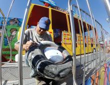 Josh Fecteau sands down the surface of the wheel on the Crazy Bus at the Bloomsburg fairgrounds Wednesday afternoon while preparing to paint it. 