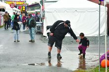 Press Enterprise/Jimmy May Mike Graaf reaches for the hand of his nephew Connor Arner, 3, who is playing in a mud puddle along 5th Street and D Ave on the Bloomsburg Fairground Monday afternoon. 