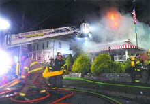 Firefighters from Mocananqua and Berwick lay hoseline as flames erupt from the roof of a home at 80 S. Main St. in Shicksinny Saturday morning.