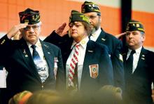 Benton VFW Post 8317 members, from left, Robert Saienni, Dawn Powlus, David Bartkiewicz and Bill Whitmoyer salute while the Benton High School women’s mixed ensemble sings the Star Spangled Banner during the Benton Area School District’s annual Veterans Day program in the L. Ray Appleman Elementary School gym on Monday morning. 