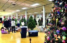 People stand next to Christmas tree decorations and partially-decorated trees.