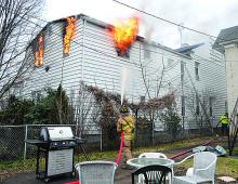 Firefighter Brent Traugh hits second-story flames with water from a hose in a neighbor's yard Friday as apartments attached to a house at 250 West Street burn in Bloomsburg.