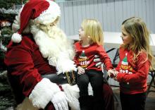 Lilly Beyer, 5, right, holds the hand of her sister Violet Beyer, 2, as she sits on Santa's knee Saturday afternoon at the Lightstreet Community Fire Company.