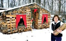 Jill Mowery stands by the log-cabin facade she constructed to dress up the woodpile at her family’s home near Hetlerville in Mifflin Township. She also decorated the log cabin for Christmas and said she has asked family members to take wood from the back of the pile. 