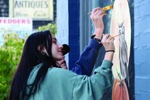 Drew Mumich/ Press Enterprise Columbia County Christian School Juniors Camille Cunningham, 15 (left) and Lyman Runkle,16 (right) puts the finishing touches on a painting on the front window of Creative Dog, Bloomsburg, on Wednesday.