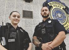Bloomsburg Police Officers Elizabeth Shampanore and Lukas Stiver stand in front of their station next to a plaque in memory of Chief Franklin Arthur Dent. He was killed in the line of duty in 1927.