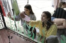 Maddy Willoughby, at left above, and Layne Winn, members of Danville Middle School’s Kindness Club, paint on the windows of The Kiddie Korner Boutique on Friday in Danville.